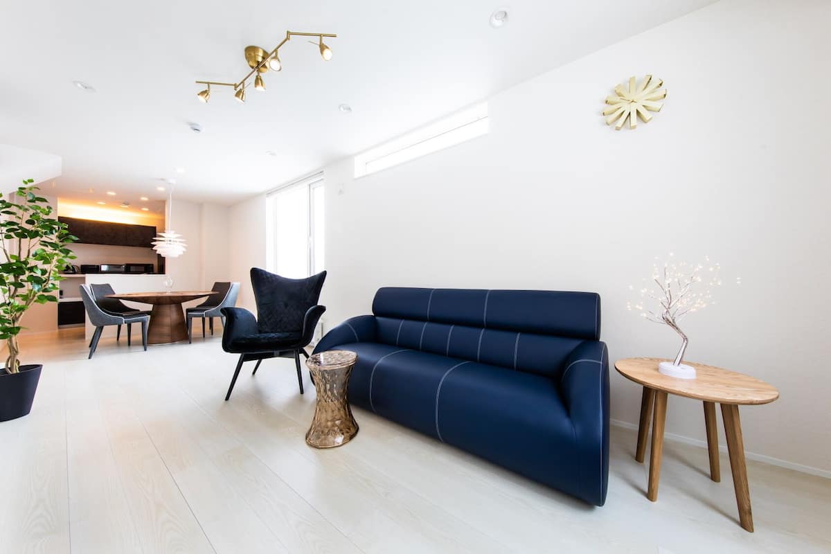 Un salon moderne avec un canapé bleu, une table à manger et des chaises. On y trouve une plante en pot et un arbre décoratif sur une table d’appoint.