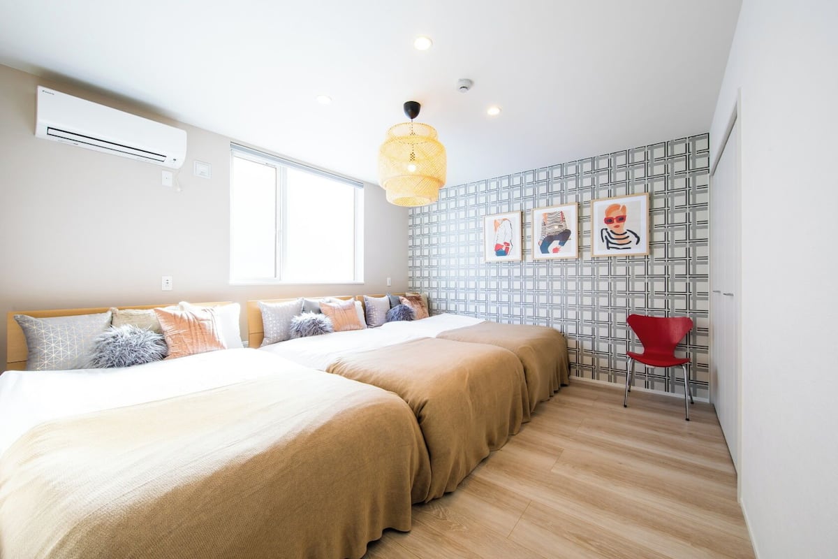 Une chambre à coucher avec un lit, une fenêtre, un climatiseur fixé au mur, un luminaire suspendu et une chaise rouge.