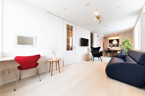 A modern living room with a red chair, a dark sofa, a TV mounted on the wall, and a dining area with a table and chairs. - Terrace Toyohira (Sapporo)