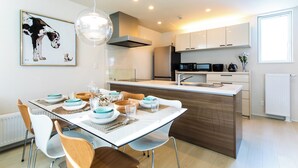 A modern kitchen with white cabinets, a central island, and a dining area with a glass table and chairs. - Terrace Toyohira (Sapporo)