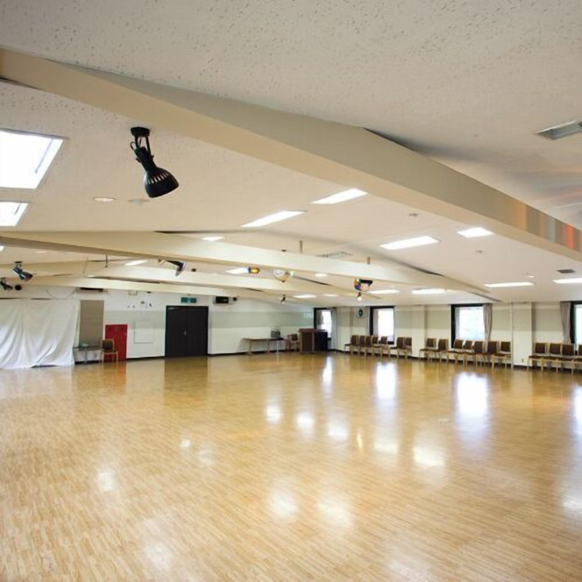 A spacious room with a high ceiling, large windows, and a wooden floor.