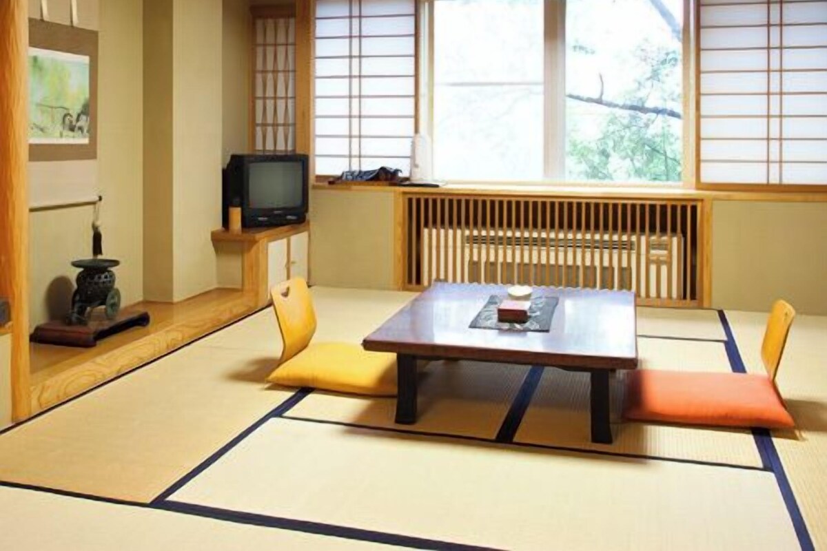 Una habitación con esteras de tatami, una mesa baja, cojines, un televisor y un radiador.