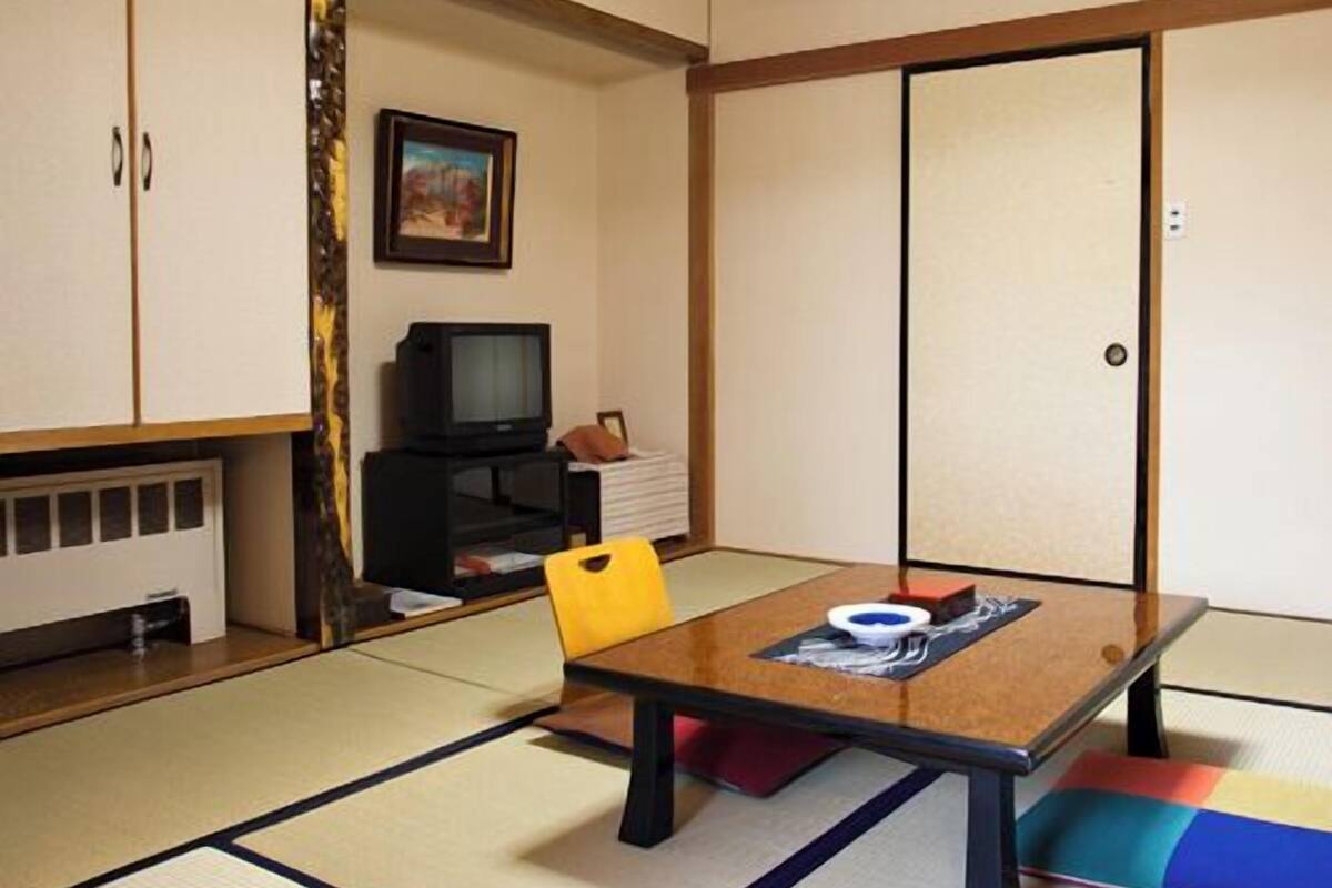 Ein traditioneller japanischer Raum mit Tatami-Böden, einem niedrigen Tisch, einem Fernseher und Schiebetüren.