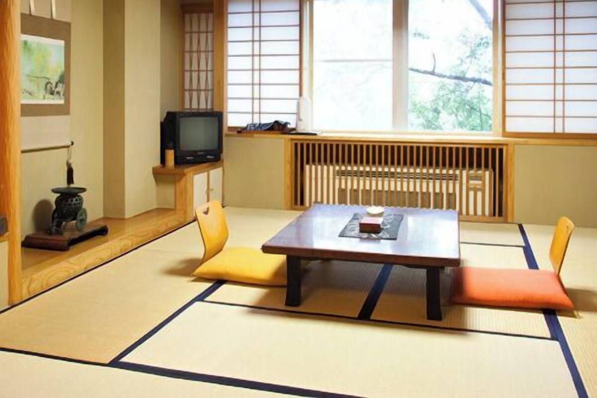 Ein Raum mit Tatami-Matten, einem niedrigen Tisch, Kissen, einem Fernseher und einem Heizkörper.
