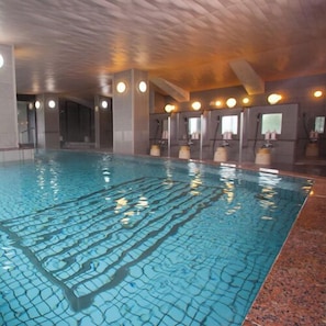 An indoor swimming pool with clear water, a tiled floor, and multiple shower areas.