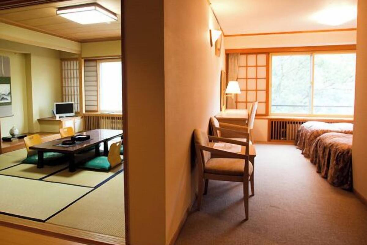 Ein traditioneller japanischer Raum mit Tatami-Bodenbelag, einem niedrigen Tisch, Stühlen, einem Bett und einem Fenster mit Aussicht.