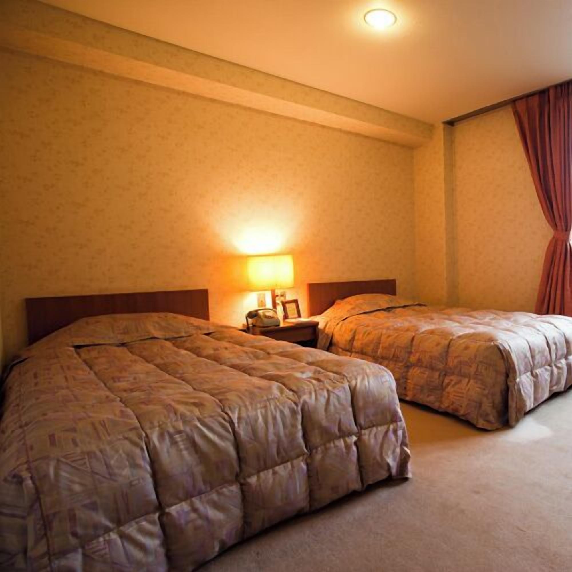 Une chambre d’hôtel avec deux lits, une table de chevet, une lampe et une fenêtre avec des rideaux.