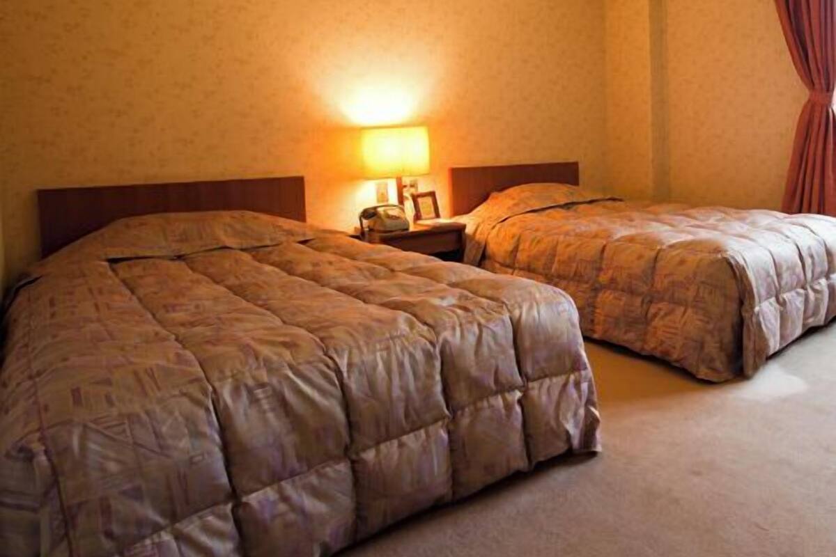 Ein Hotelzimmer mit zwei Betten, einem Nachttisch, einer Lampe und einem Fenster mit Vorhängen.