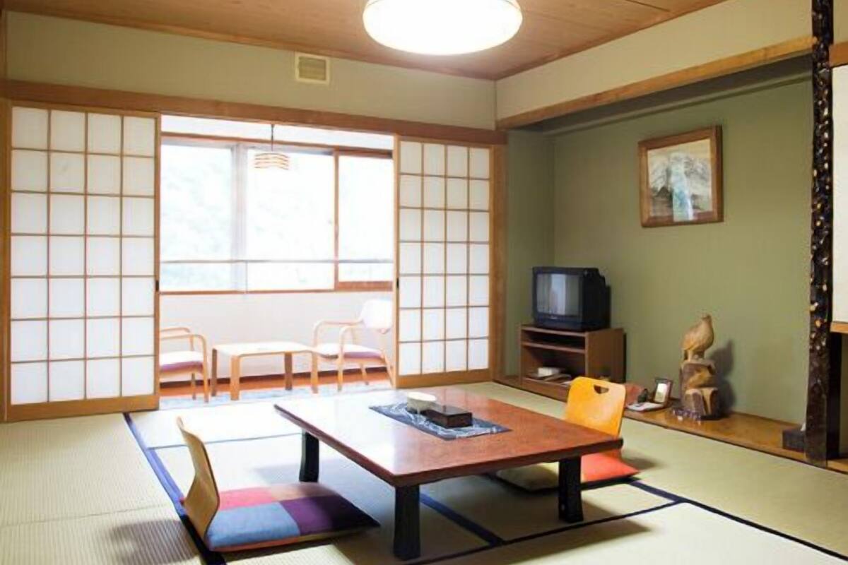 Ein traditioneller japanischer Raum mit Tatami-Boden, einem niedrigen Tisch und einem Fernseher.