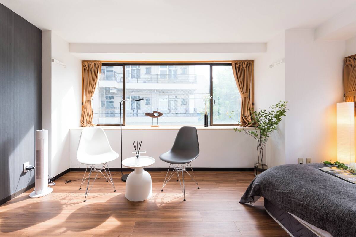 Ein modernes Hotelzimmer mit einem großen Fenster, einem Bett, einem weißen Tisch mit zwei Stühlen und einem Heizlüfter.