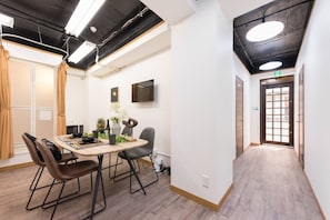 A modern hotel room with a wooden floor, a dining table with chairs, a flat-screen TV, and a door with a glass panel. - Tora Hotel Rikugien (Tokyo)