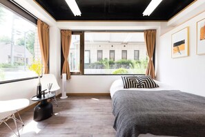 Una habitación de hotel moderna con un ventanal grande, una cama, una silla y una mesita.