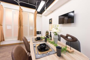 Un comedor moderno con una mesa de madera preparada para dos personas, un televisor montado en la pared y un ventanal corredero que da a un balcón.