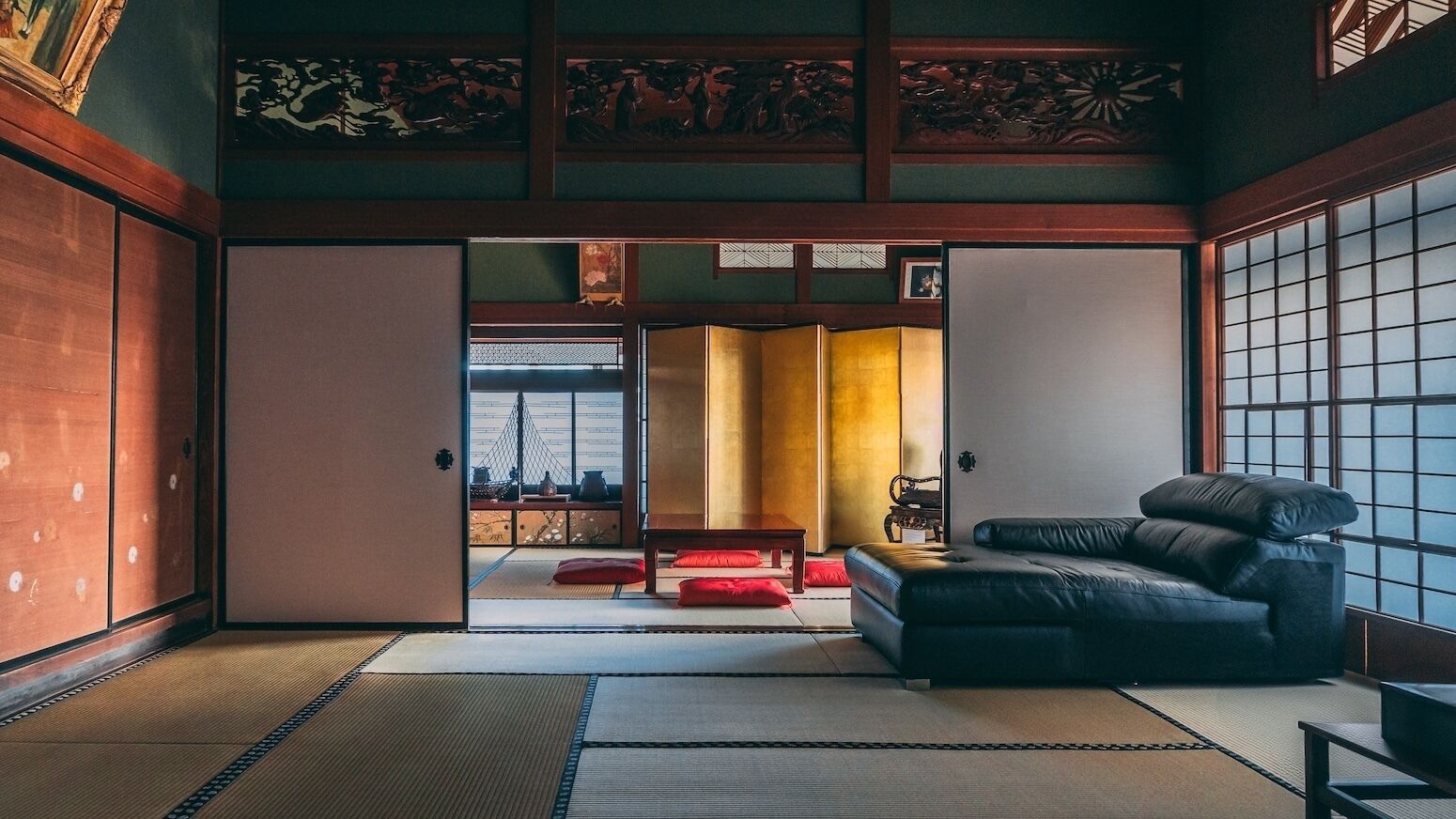 Una habitación tradicional japonesa con suelo de tatami, un sofá de cuero negro y puertas correderas.