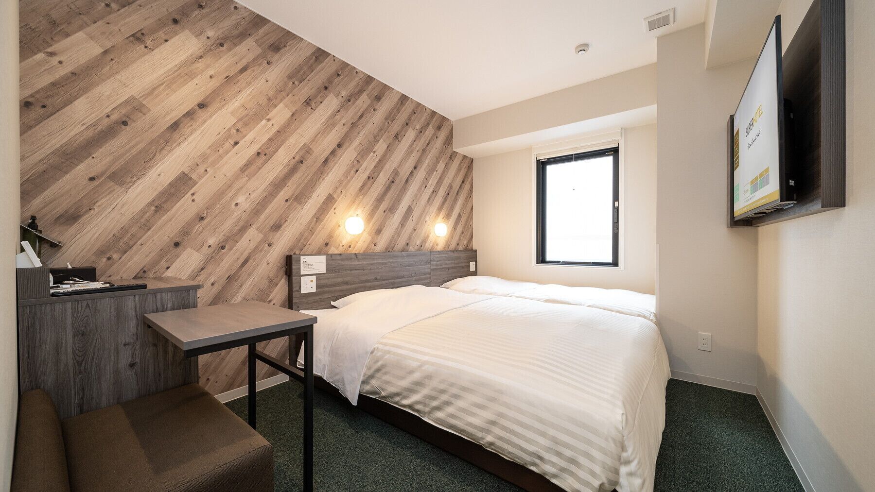 Une chambre d’hôtel comprenant un lit, un bureau, une chaise, un mur décoratif en bois, une fenêtre et un téléviseur fixé au mur.