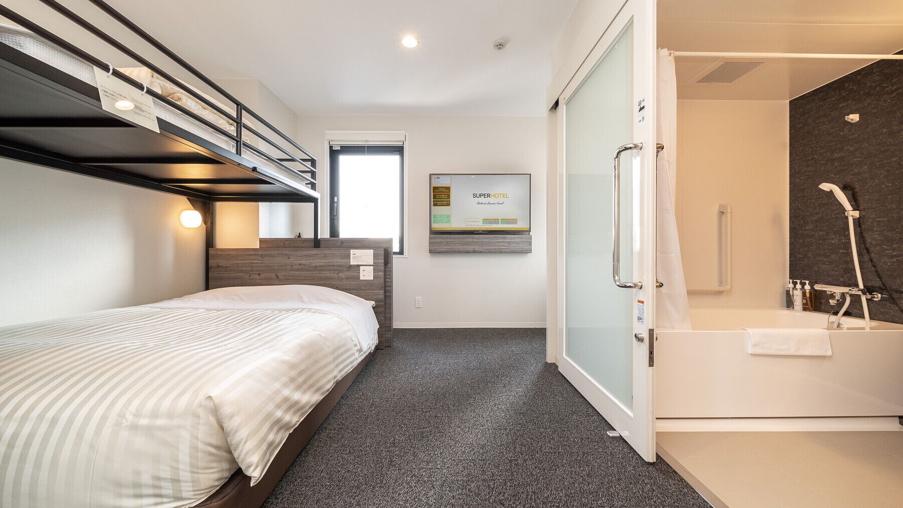 Une chambre d’hôtel avec un lit superposé, une douche avec une porte en verre et une affiche au mur.
