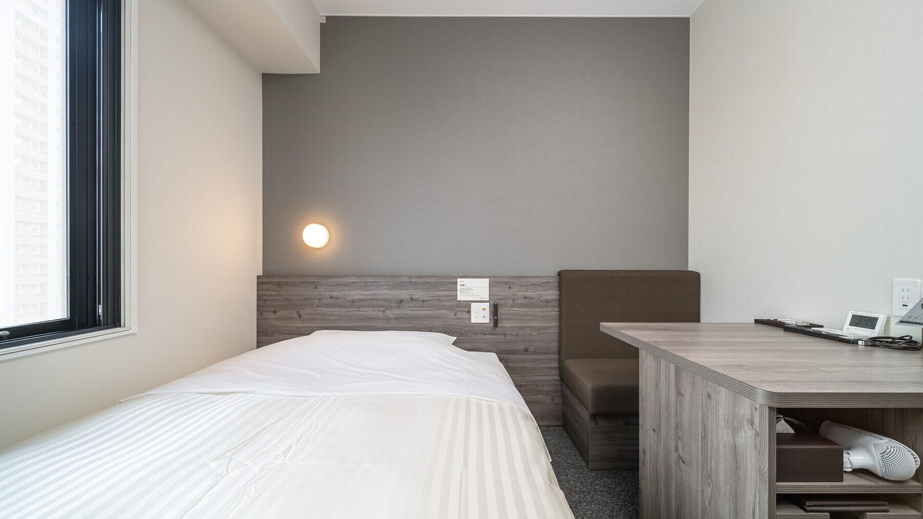 Une chambre d’hôtel comprenant un lit, un bureau avec une chaise, une lampe fixée au mur et une fenêtre.