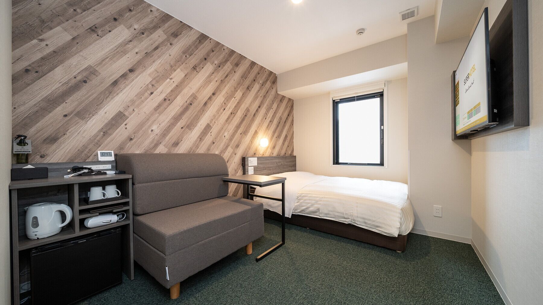 Une chambre d’hôtel compacte comprenant un canapé, un petit bureau, un lit, une télévision et un mur en bois.