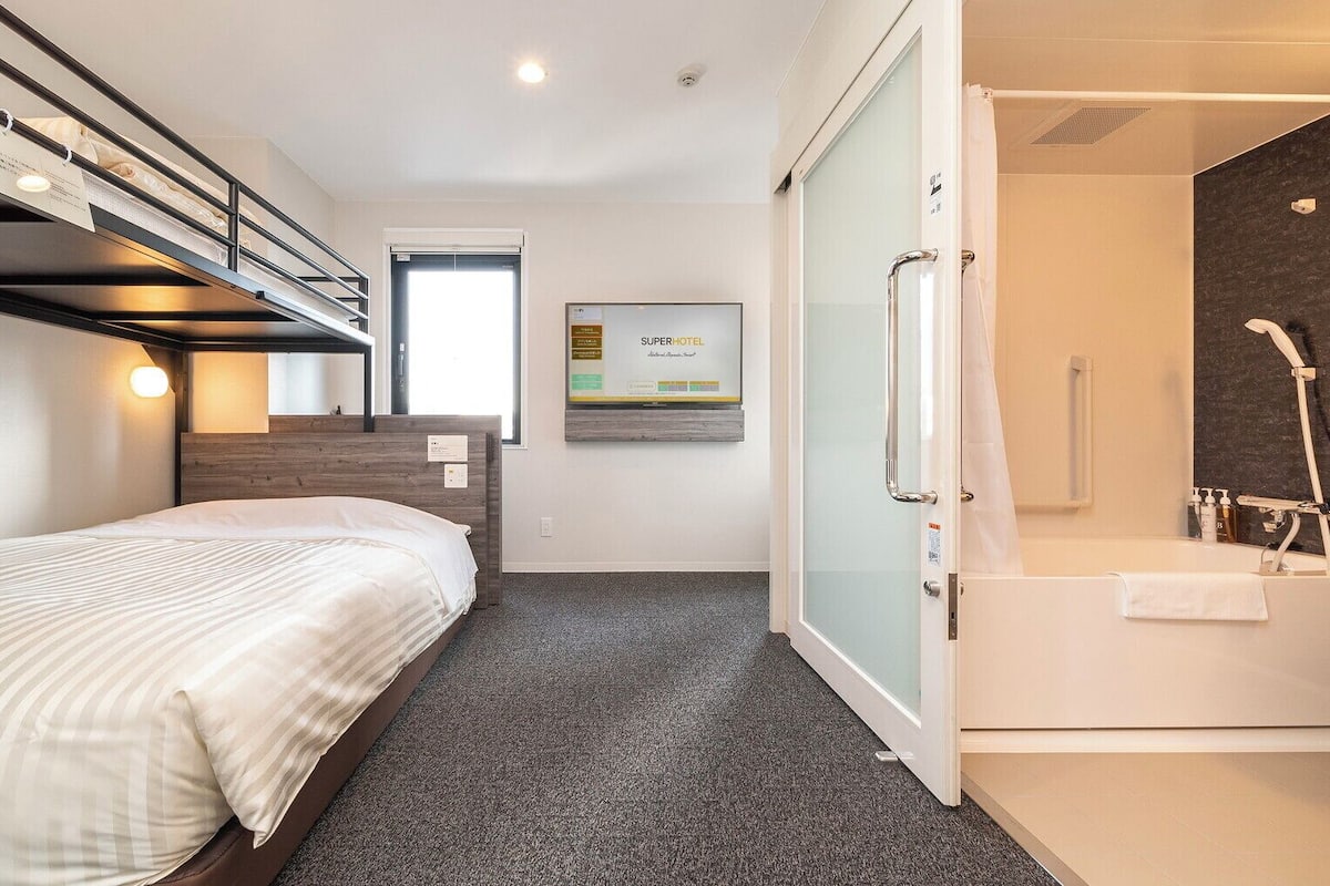 A hotel room with a bunk bed, a shower with a glass door, and a poster on the wall.