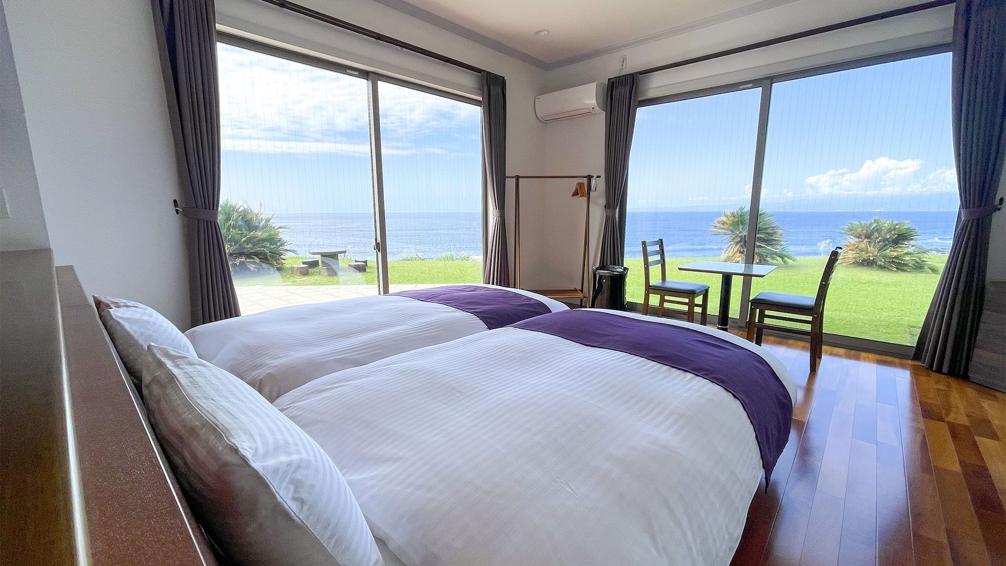 A hotel room with a large bed, a table, and chairs, and a view of the ocean.