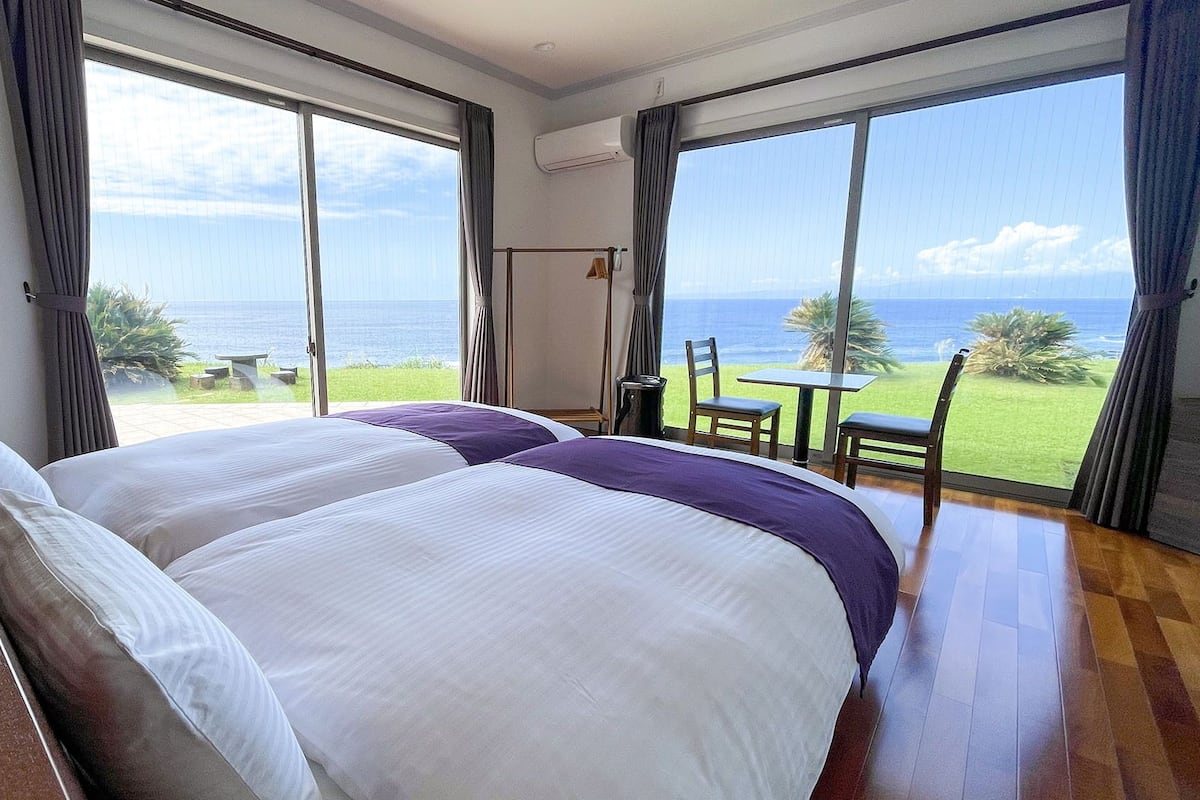 A hotel room with a large bed, a table, and chairs, and a view of the ocean.