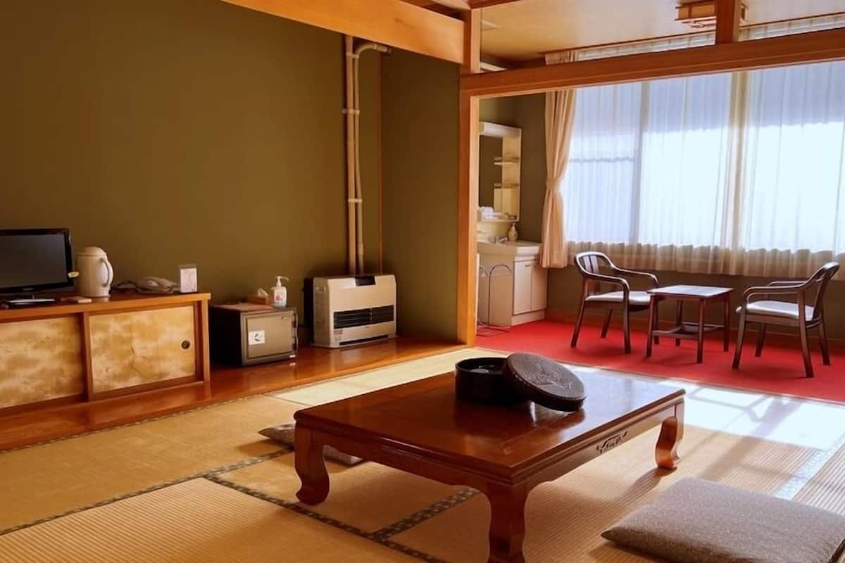 Et traditionelt japansk værelse med tatamimåtter, et lavt bord, en sofa og et fjernsyn.