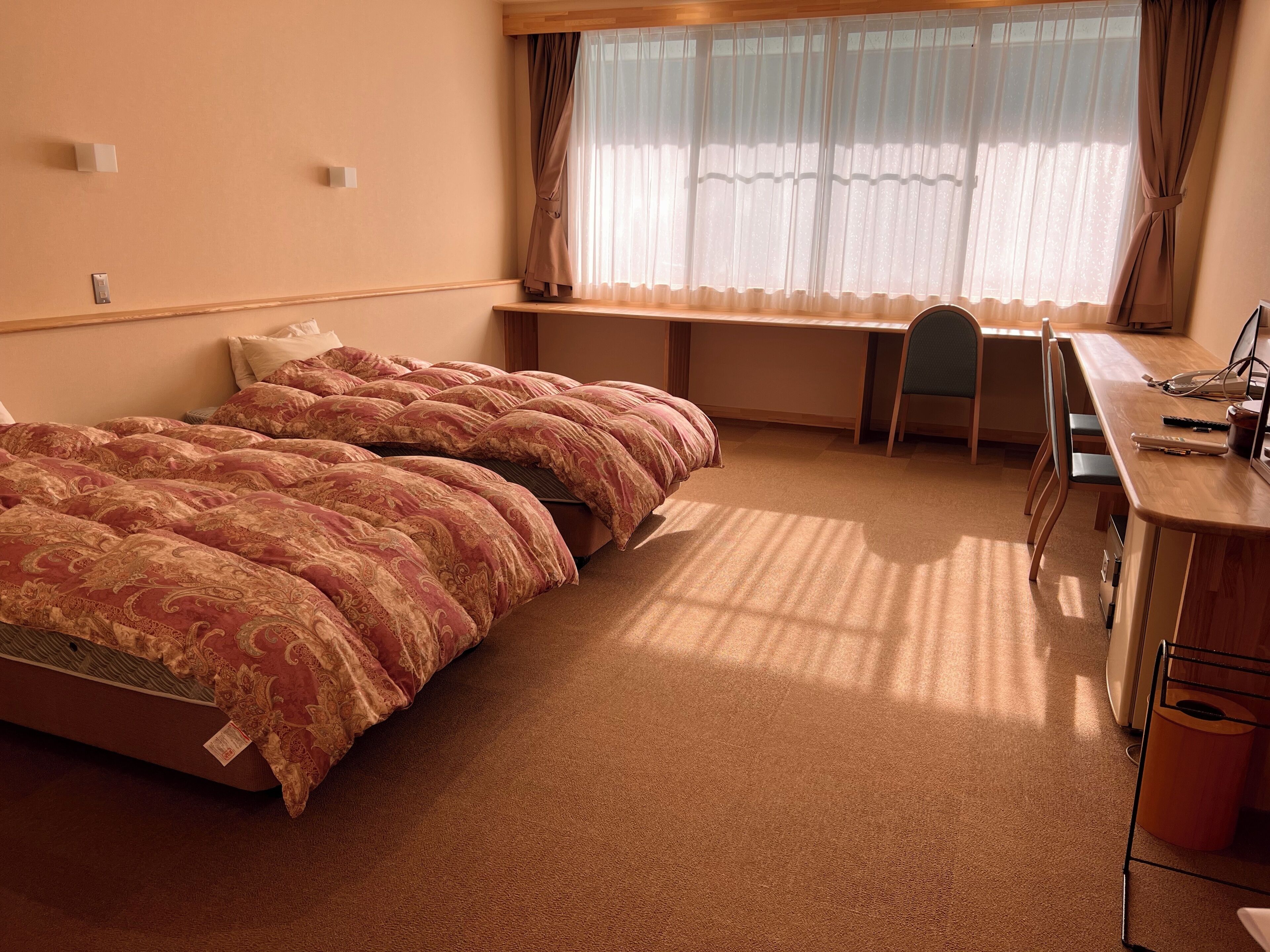 Hotellihuone, jossa on sänky, työpöytä, tuoli ja ikkuna, jossa on verhot.