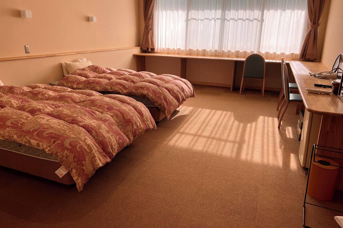 Et hotelværelse med seng, skrivebord, stol og et vindue med gardiner.