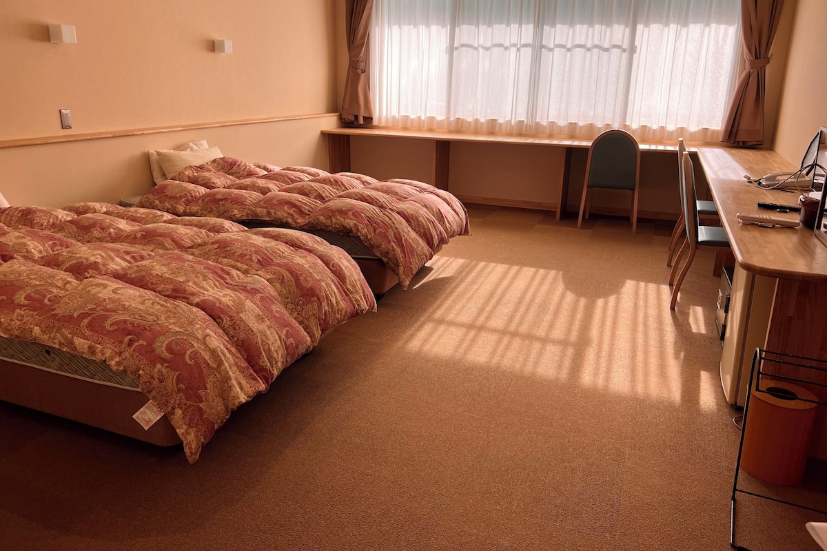 Hotellihuone, jossa on sänky, työpöytä, tuoli ja ikkuna, jossa on verhot.