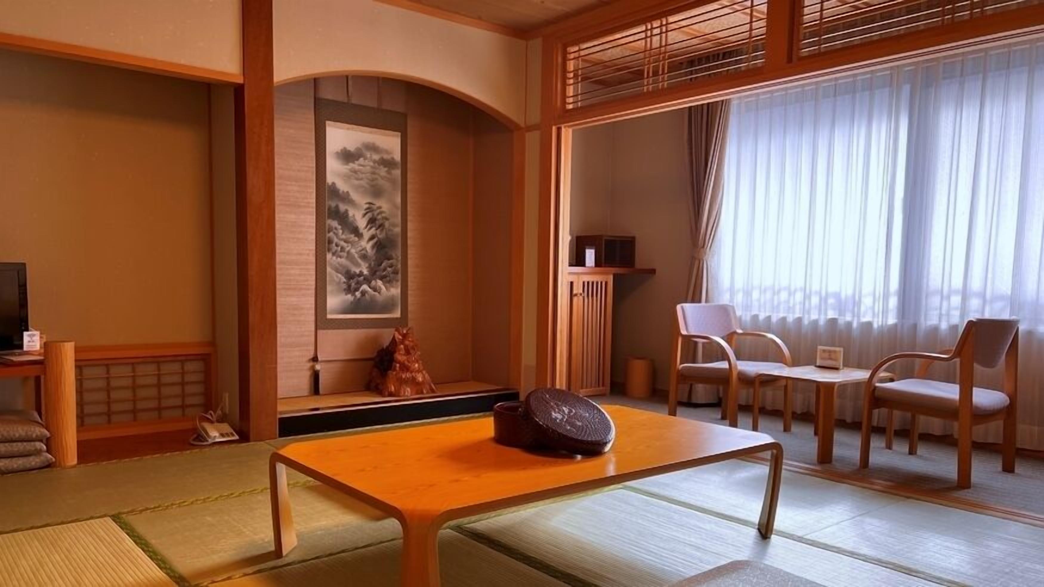 A traditional Japanese room with tatami flooring, a low table with a decorative item, a painting, and a view through sheer curtains.