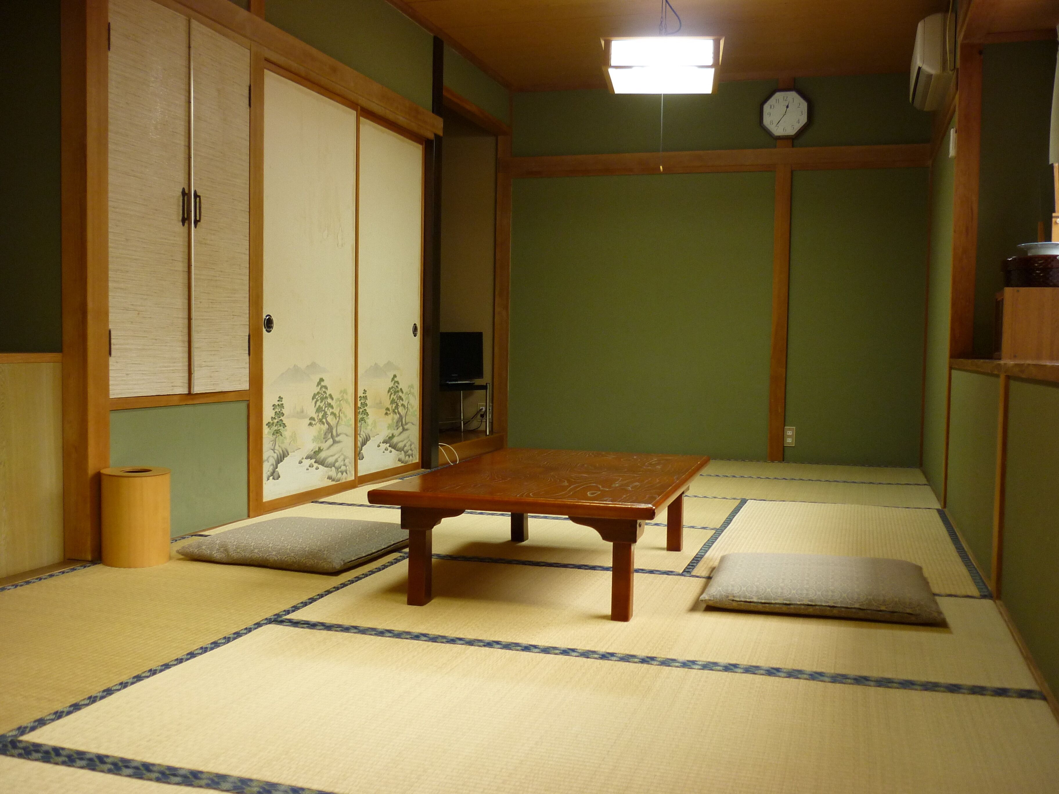 Tatami-mattoilla päällystetty huone, jossa on matala puupöytä, futon-patja, televisio ja perinteinen japanilainen liukuovi.