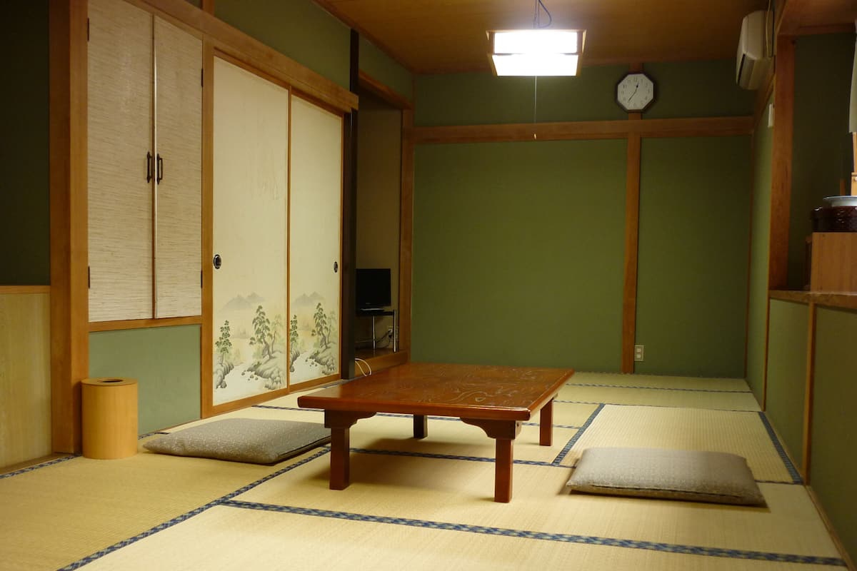 Et rum med tatamimåtter, et lavt træbord, en futon, et fjernsyn og en traditionel japansk skydedør.