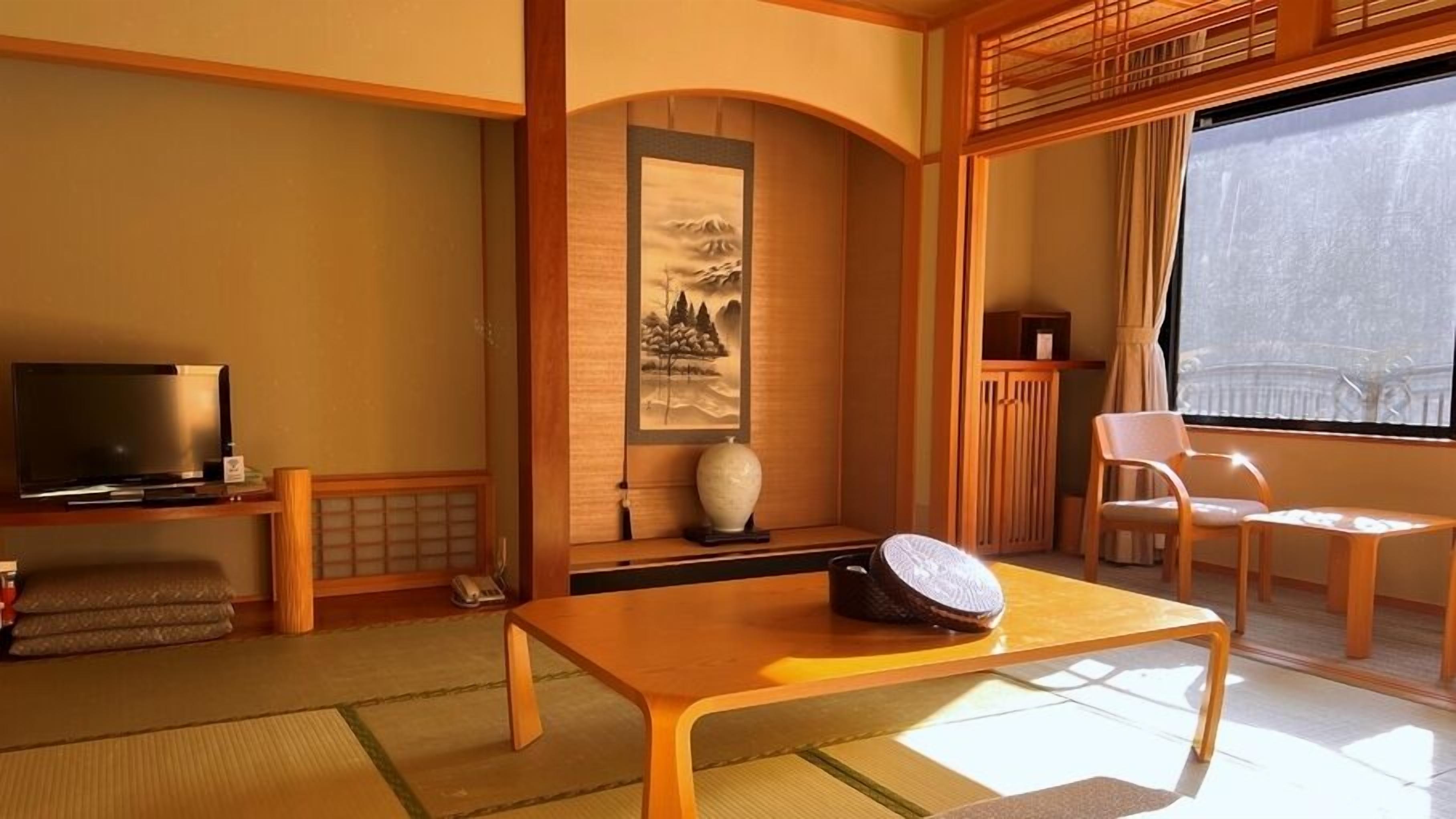 A traditional Japanese-style room with tatami flooring, a television, a painting, and a wooden table.