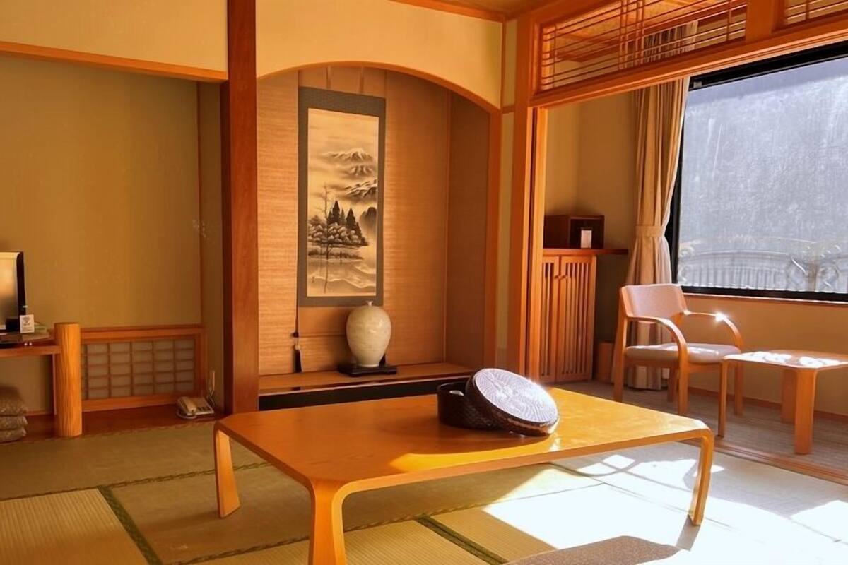 Et traditionelt japansk værelse med tatamimåtter, et fjernsyn, et maleri og et træbord.