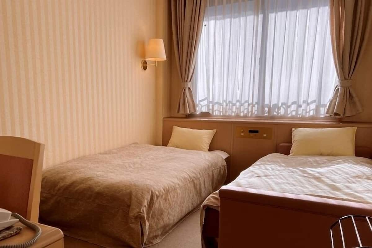 Et hotelværelse med to senge, et natbord med lampe, en telefon og et vindue med gardiner.