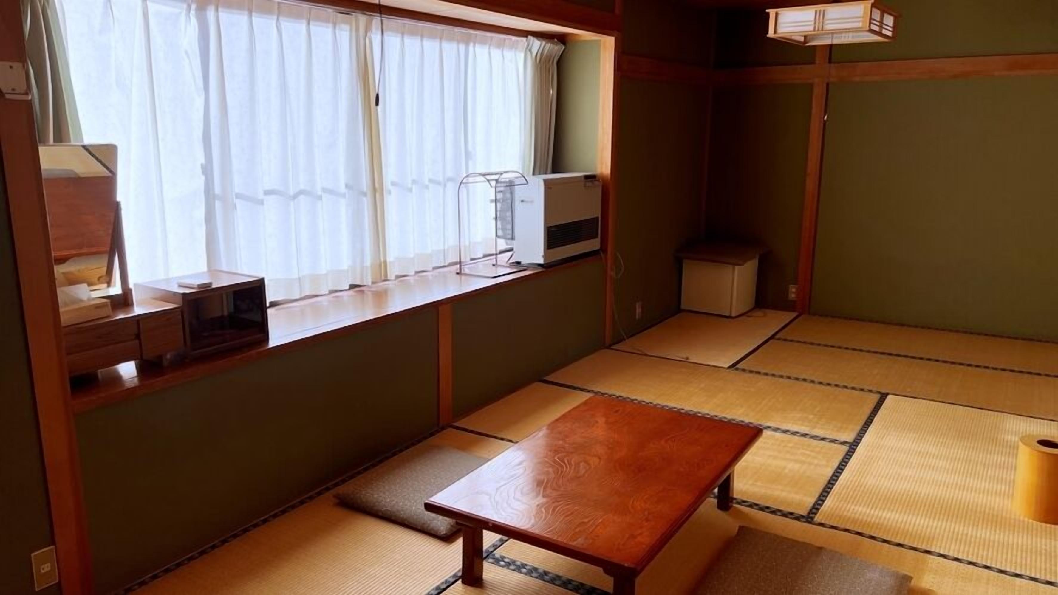 A tatami mat room with a low table, a window with curtains, a heater, and a small cabinet.