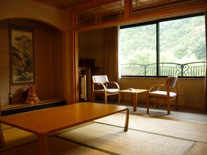 A traditional Japanese room with tatami flooring, a low table, two chairs, a small table with a cup, and a view of a forest through a balcony. - Senryuso (Ina)