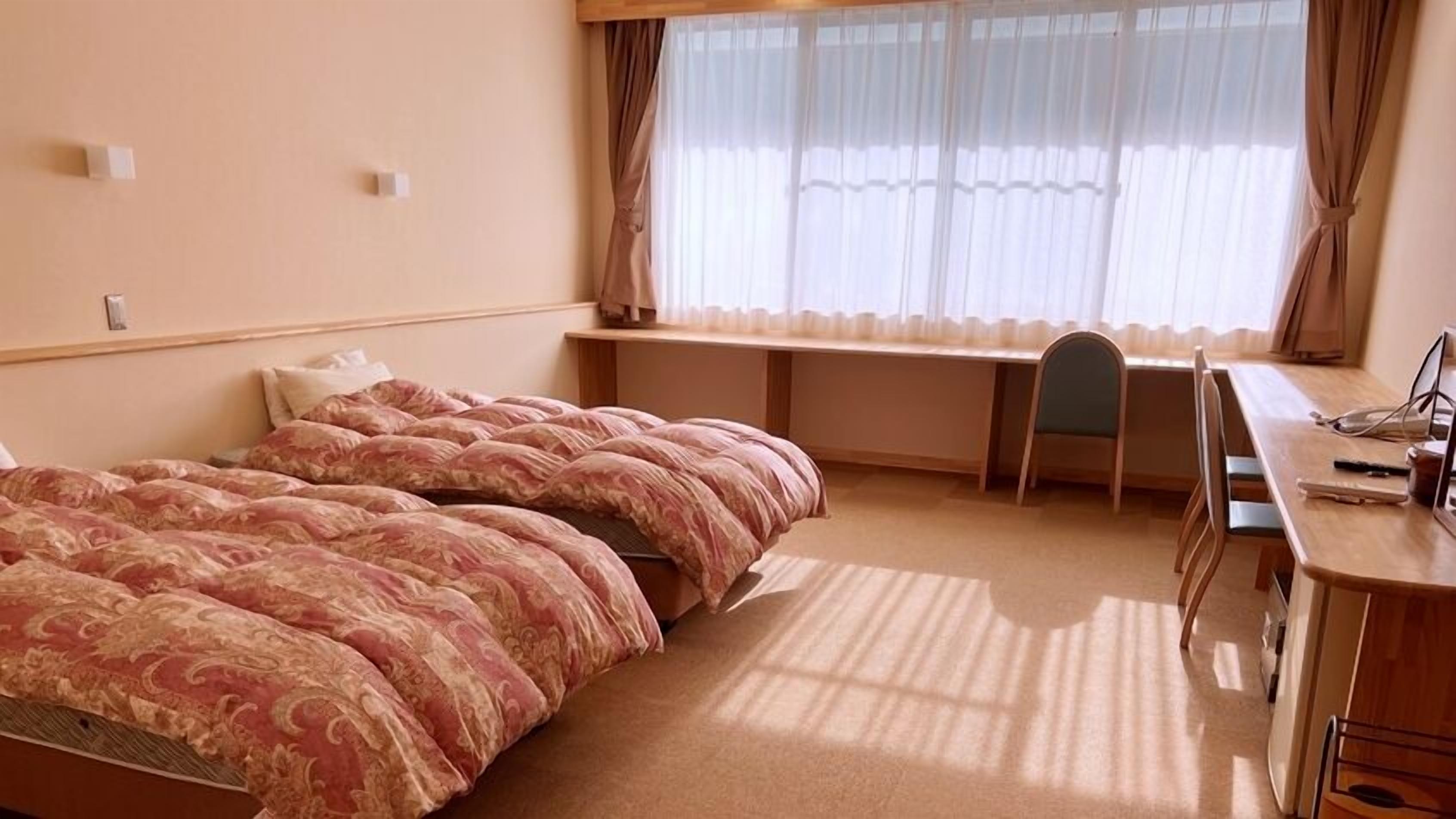 A hotel room with a bed, desk, chair, and a window with curtains.