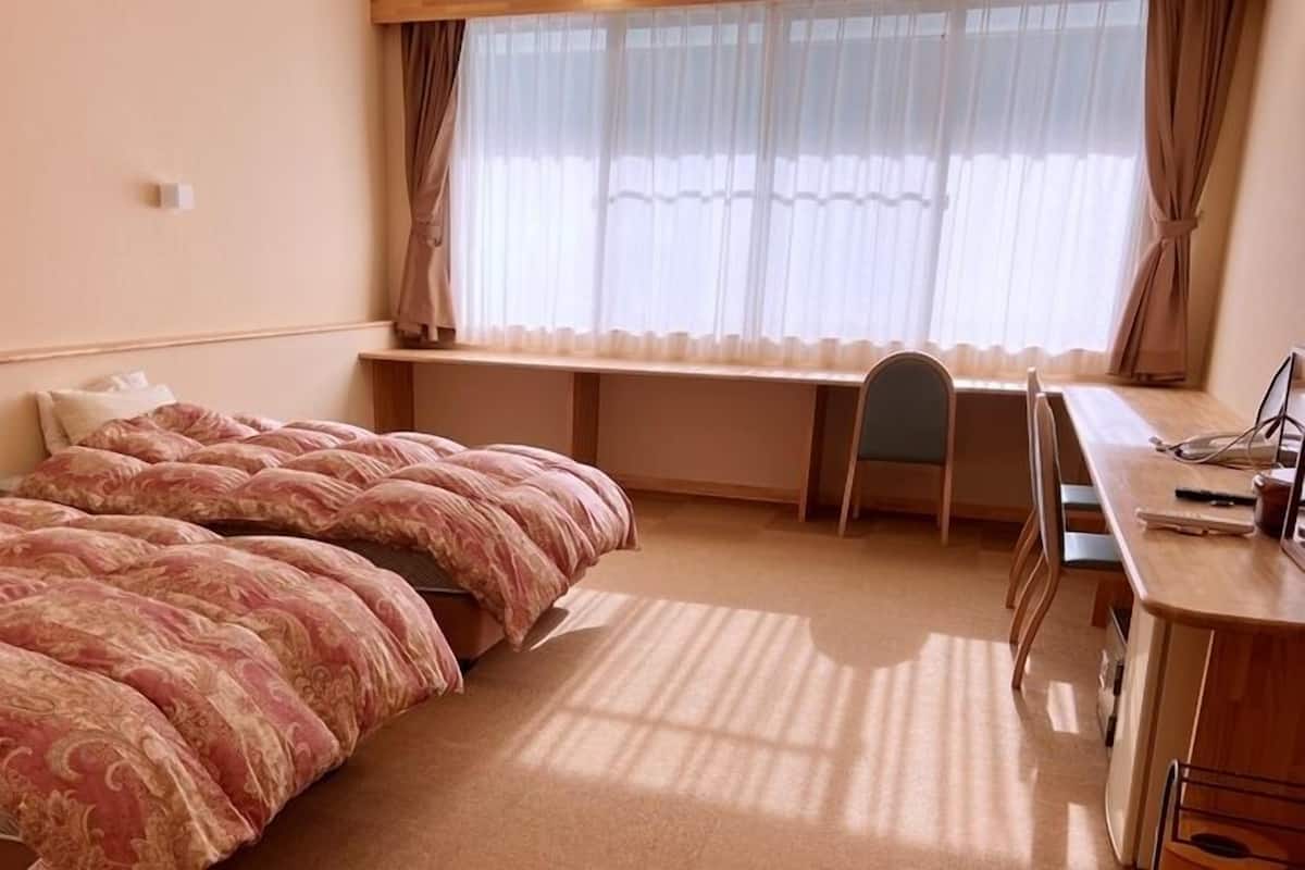 Et hotelværelse med seng, skrivebord, stol og et vindue med gardiner.