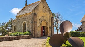A stone church with an arched doorway and a large propeller sculpture in front. - Stunning home in SAINT VAAST LA HOUGUE with WiFi (SAINT VAAST LA HOUGUE)