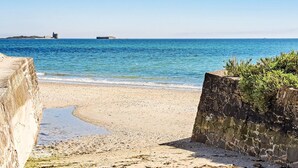 A coastal beach with a clear view of the sea, a stone wall, and a distant structure. - Stunning home in SAINT VAAST LA HOUGUE with WiFi (SAINT VAAST LA HOUGUE)