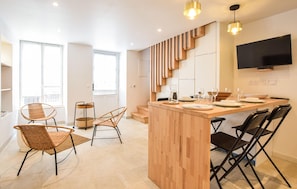 A modern kitchen with a wooden island, black chairs, and a flat-screen TV.