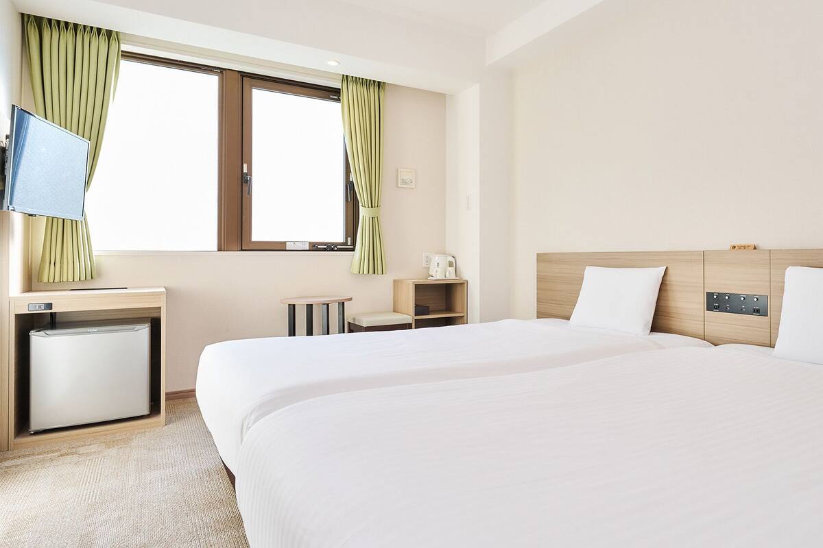 A hotel room with a bed, a desk with a refrigerator, a coffee maker, and a TV.