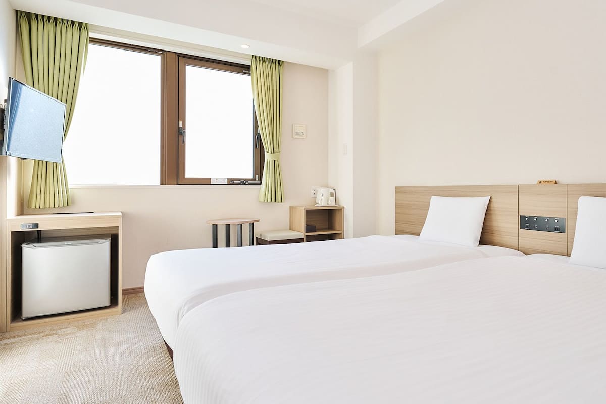 Hotellihuone, jossa on sänky, työpöytä, jossa on jääkaappi, kahvinkeitin ja televisio.
