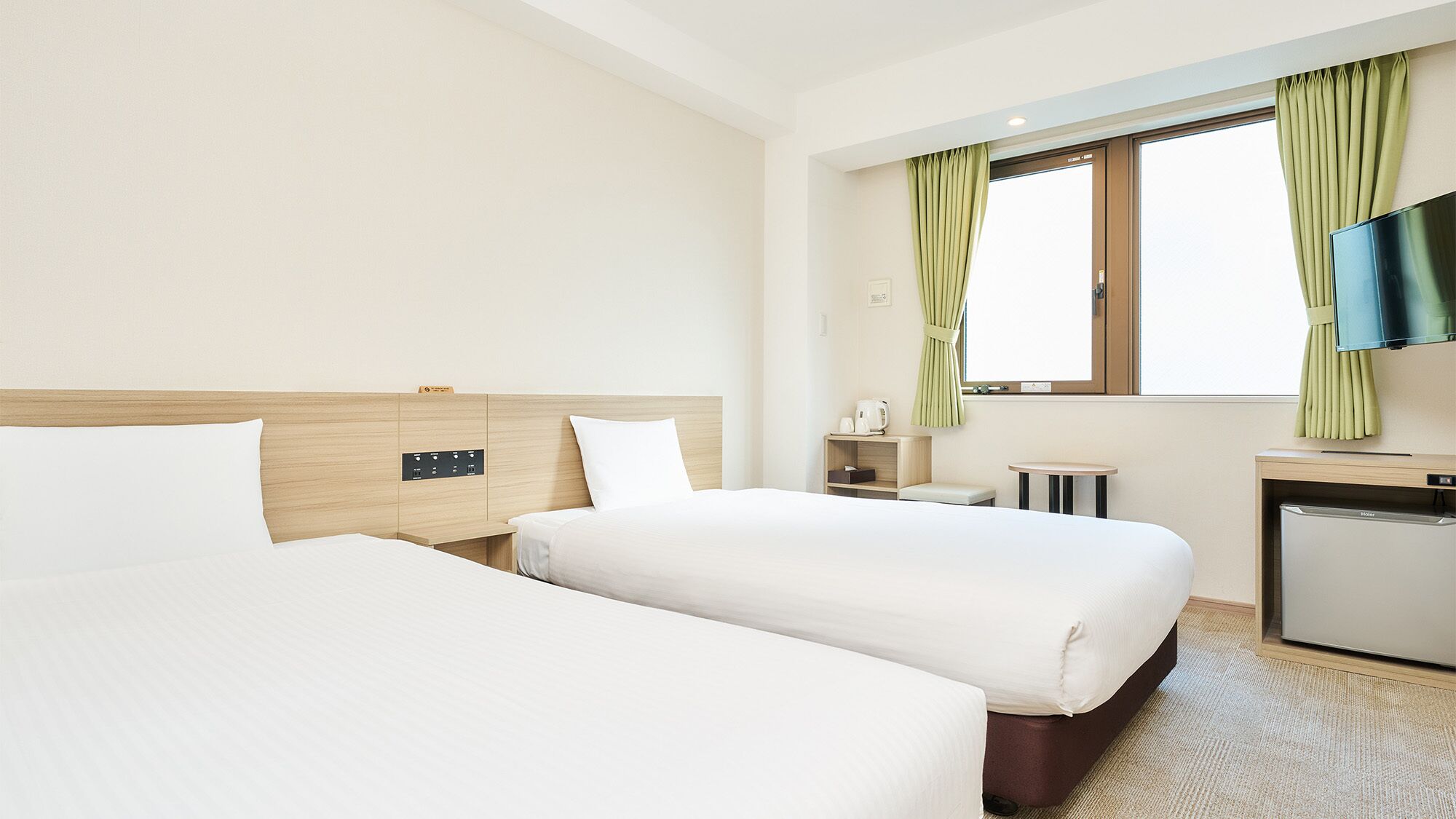 Hotellihuone, jossa on kaksi sänkyä, pieni työpöytä, televisio ja ikkuna, jossa on verhot.