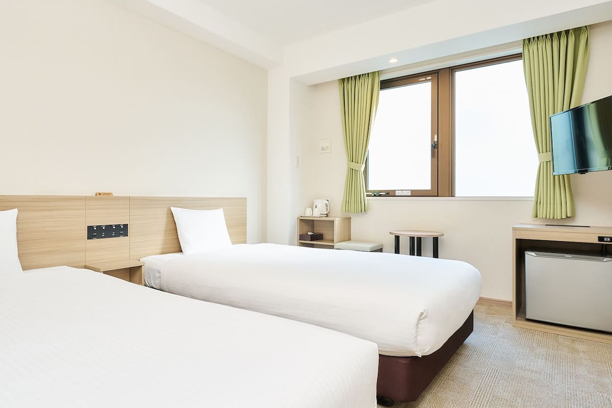 Hotellihuone, jossa on kaksi sänkyä, pieni työpöytä, televisio ja ikkuna, jossa on verhot.