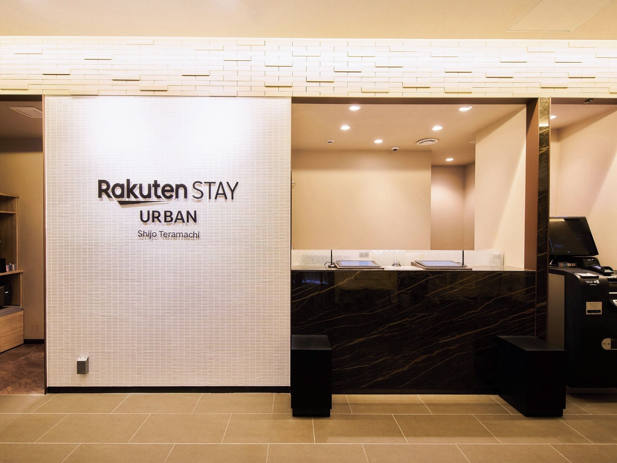 Vastaanottotiski, jossa on kyltti, jossa lukee ”Rakuten Stay URBAN”, ja nimikyltti, jossa lukee ”Shijo Teramachi”.