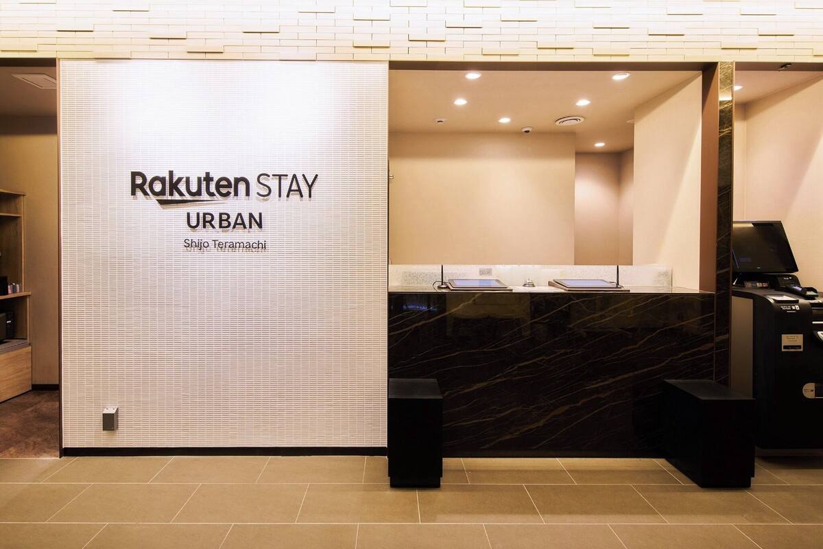 A reception desk with a sign reading "Rakuten Stay URBAN" and a nameplate "Shijo Teramachi".