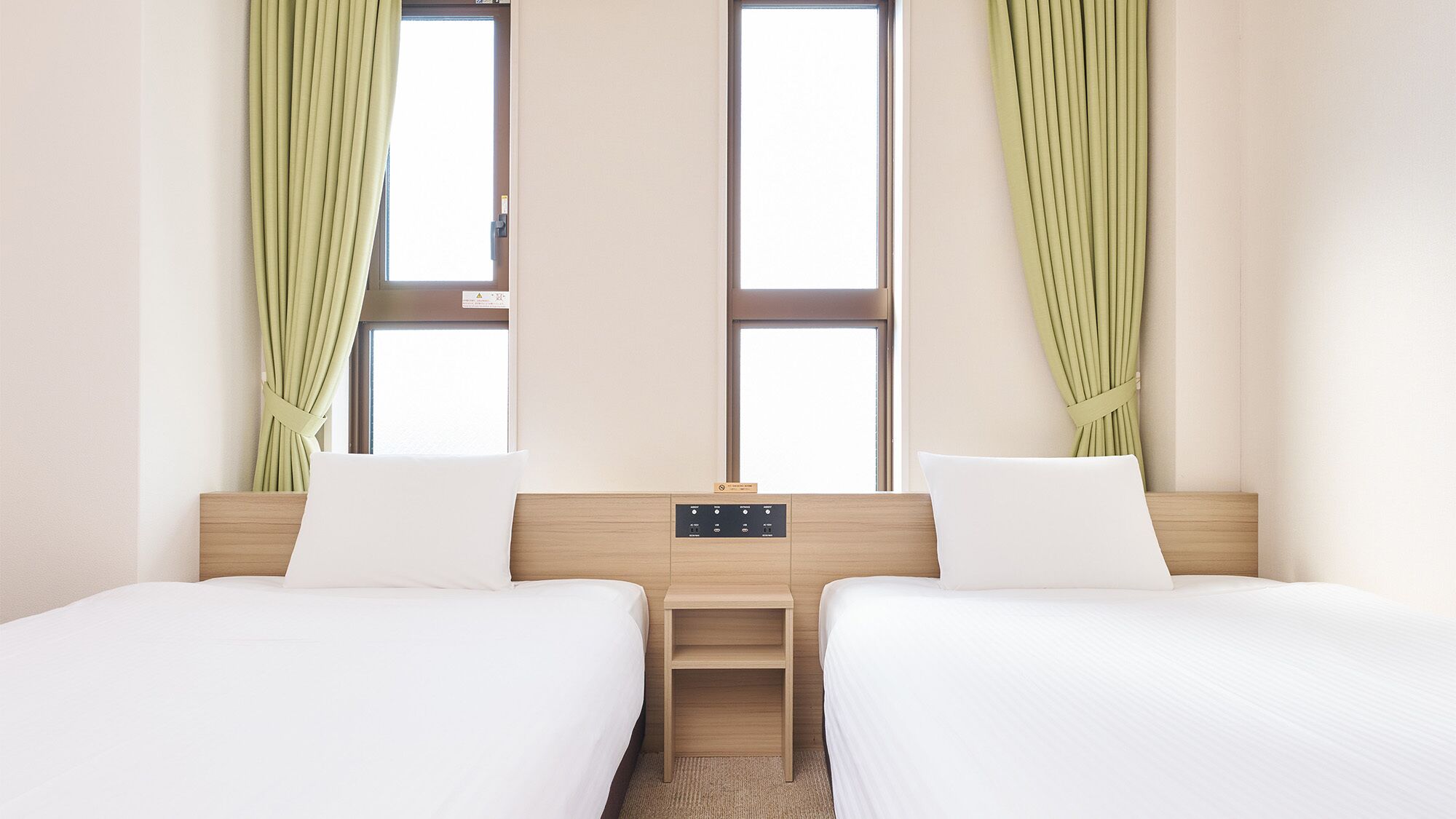 Hotellihuone, jossa on kaksi sänkyä, yöpöytä ja ikkuna, jossa on verhot.
