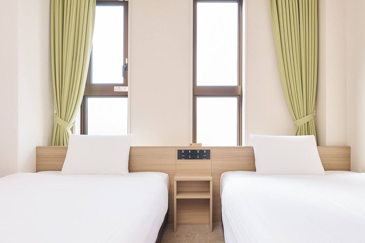 A hotel room with two beds, a nightstand, and a window with curtains.